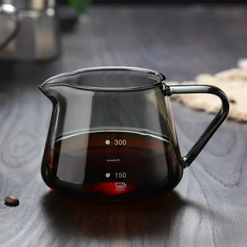 A sleek dark-tinted glass coffee pot with black handle and measurement markings for 150ml and 300ml used as a kitchen carafe