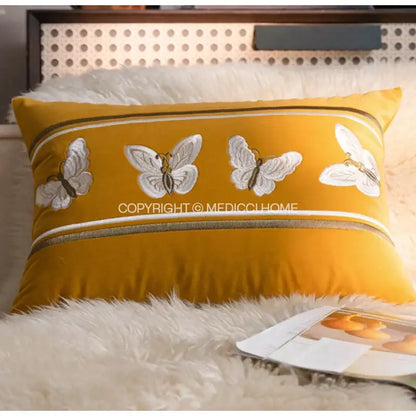 A mustard-yellow french night velvet throw pillow with embroidered white butterflies and striped decorative borders