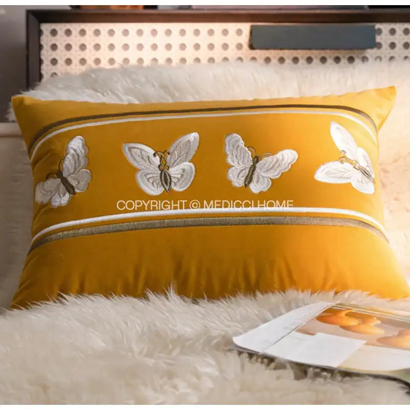 A mustard-yellow french night velvet throw pillow with embroidered white butterflies and striped decorative borders