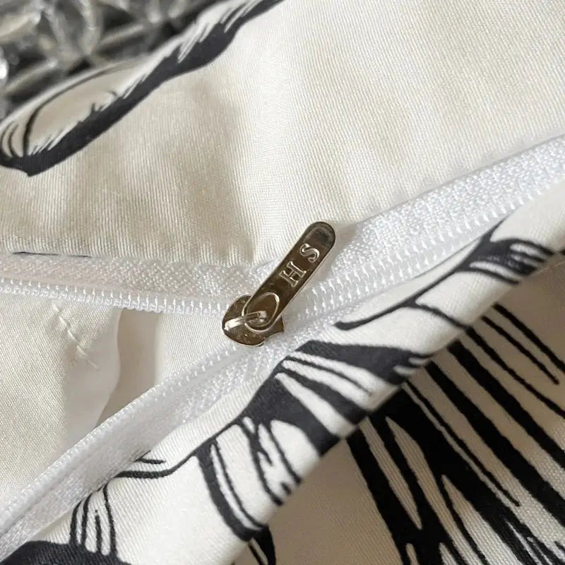 A metallic gold-toned zipper pull with hs engraved on a french vintage black and cream ruffles duvet cover set