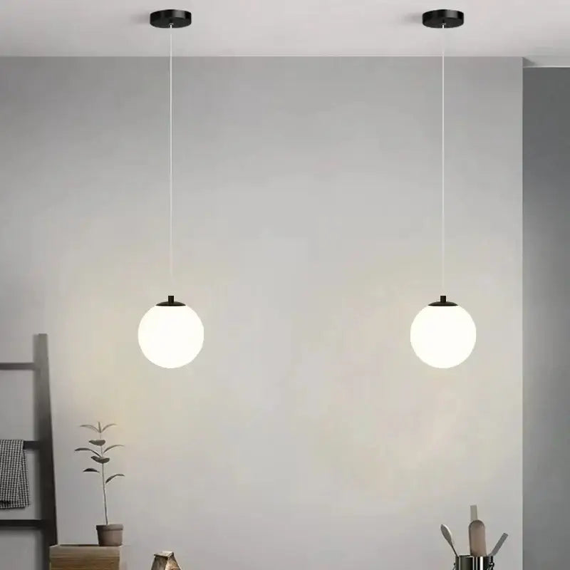 Two minimalist frosted glass pendant lights with spherical white shades and black fixtures for dining room use