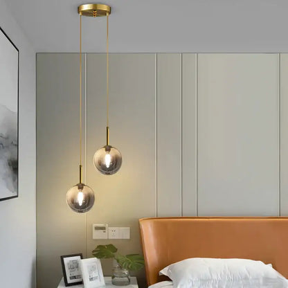 Modern brass-finished pendant light with smoke gray globe pendant light shades hanging above a bed for dining room use