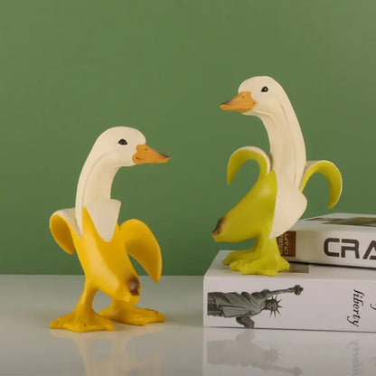 Two whimsical white resin duck sculptures with orange beaks wrapped in bright yellow banana peels banana duck sculpture