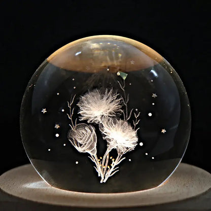 A clear crystal ball music box with etched white dandelion and rose blossoms on a rotating wooden base