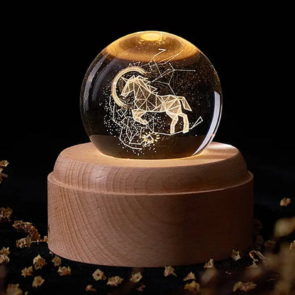 A glowing aries constellation crystal ball music box with geometric etching on a light wooden base for bedroom decor