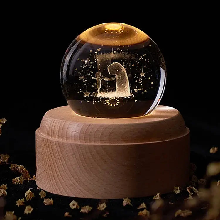 A glowing golden crystal ball music box with an engraved nativity scene on a light wood rotating base