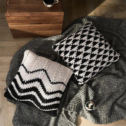 Two geo knit stripe square pillows in black white and cream black resting on a gray knit blanket for decorbites geo knit decor