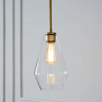 A clear glass pendant light with brass-finished rod and exposed edison bulb in geometric glass pendant lights set