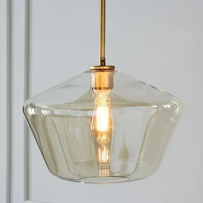 A modern pendant light with a clear faceted glass shade and brass hardware in a geometric pendant lights set for living room