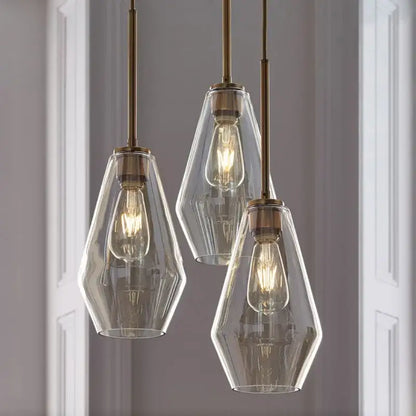 Three clear glass pendant lights with brass accents and exposed filament bulbs in a geometric pendant lights set