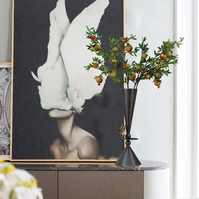 Black metallic geometric bronze vase with conical shape and gold bird detail holding artificial branch with fruits