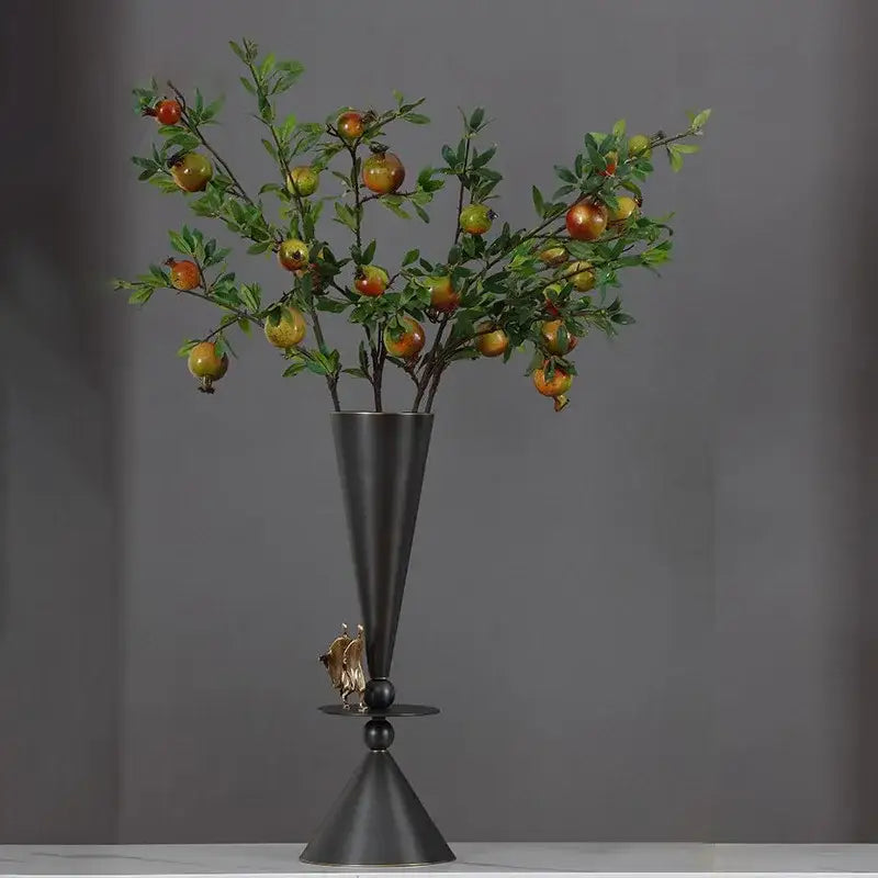 A sleek matte black geometric bronze vase with a gold figurine base holding an artificial pomegranate branch