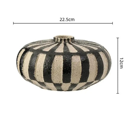 A round geometric check ceramic vase with bold black and beige vertical stripes and a textured surface for living room decor