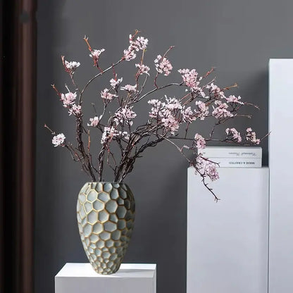 Light gray ceramic vase with geometric diamond check honeycomb pattern holding pink cherry blossom branches for decor