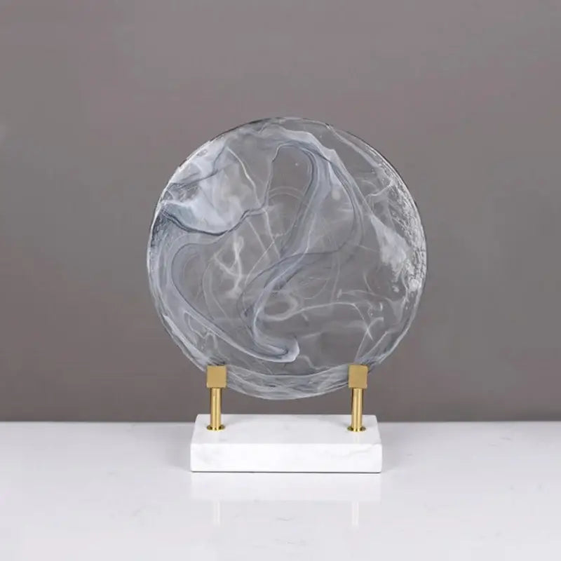 Geometric disk marble clear glass orb in translucent gray and white on marble base with gold supports for home decor
