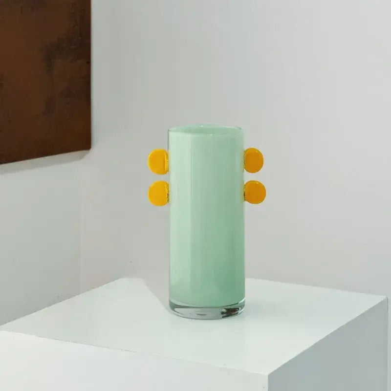 A mint-green decorbites geometric glass vase with bright yellow color patches and four circular handles for living room decor
