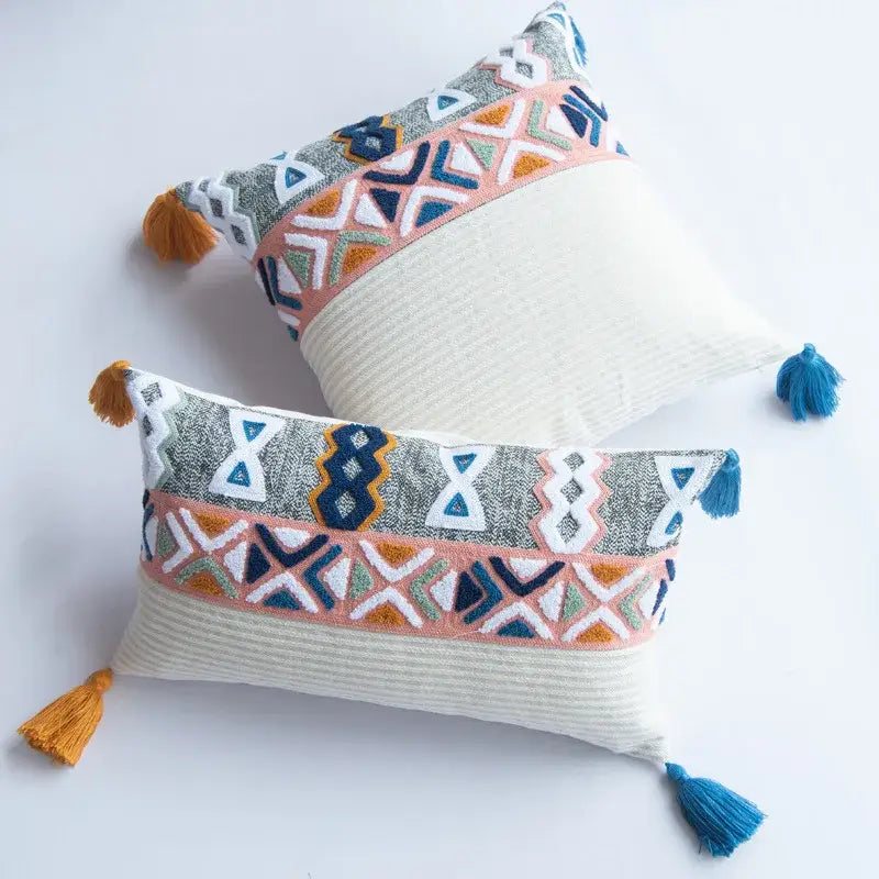 Rectangular embroidered cushion cover with multicolor geometric patterns and tassels on a textured white base