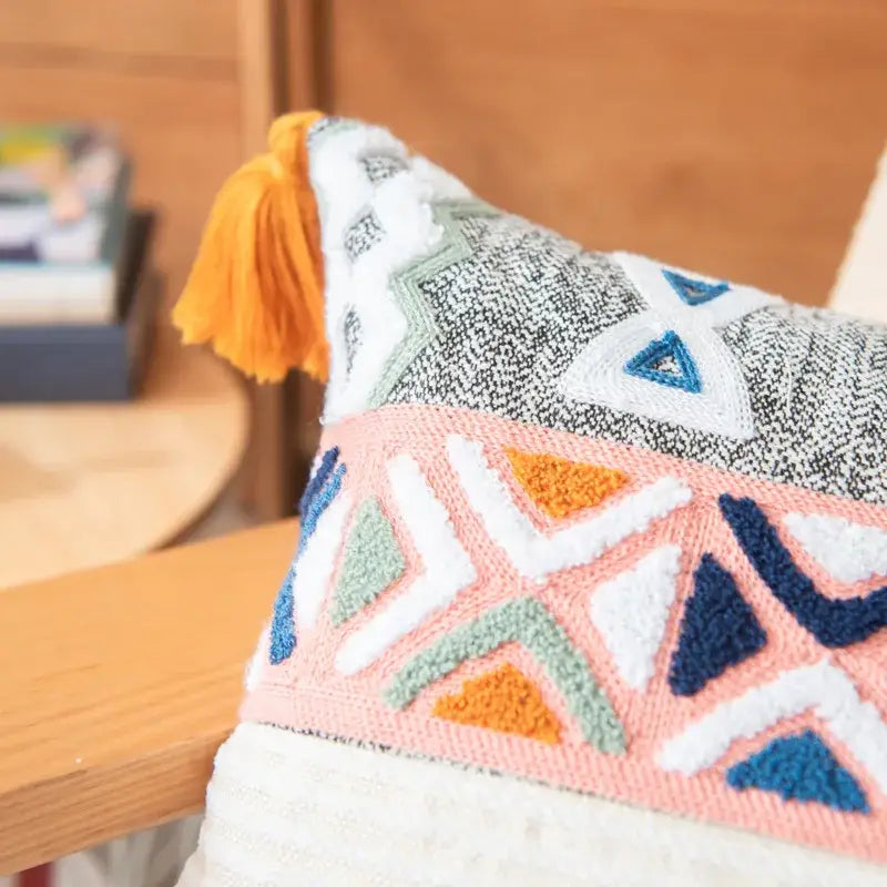 A cozy embroidered cushion cover with vibrant geometric multicolor pattern and orange tassel for living room decor