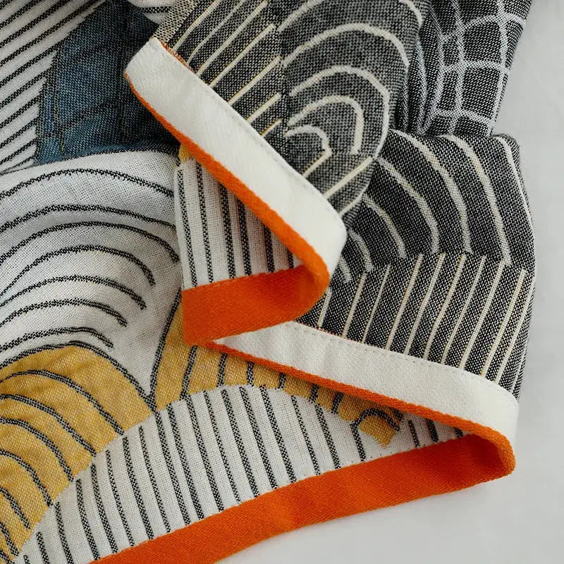 Folded decorbites cotton gauze bath towel with bold black white mustard geometric pattern and orange trimmed edge