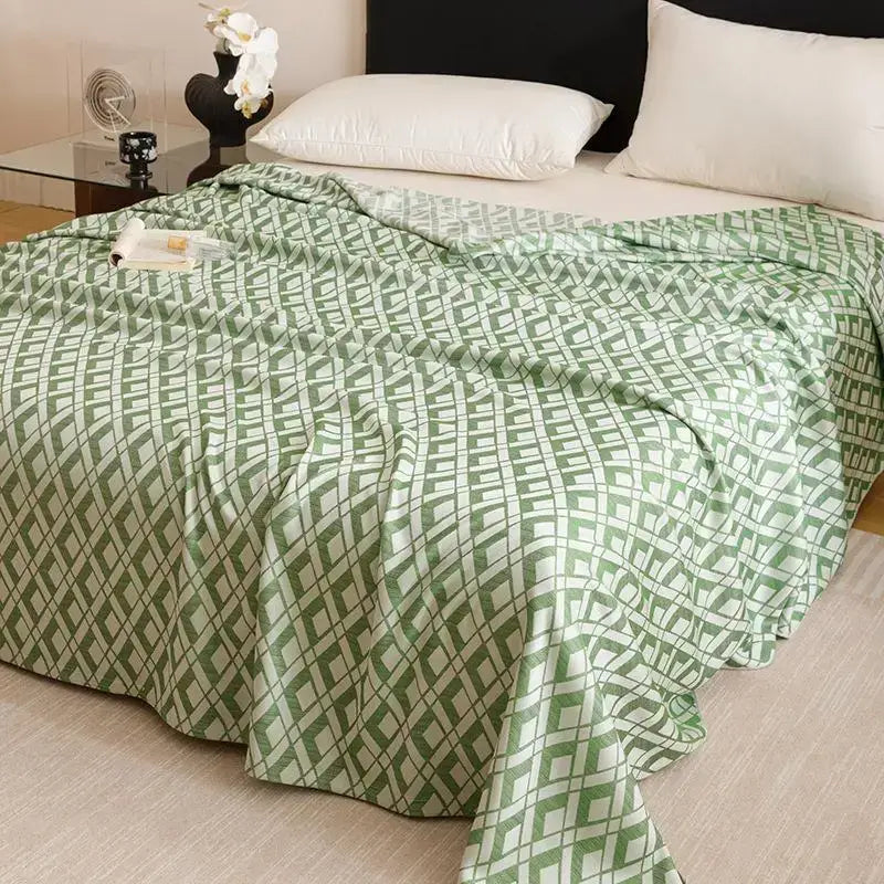 A soft green and white geometric-patterned decorbites bamboo fiber summer blanket draped on a neatly made bed