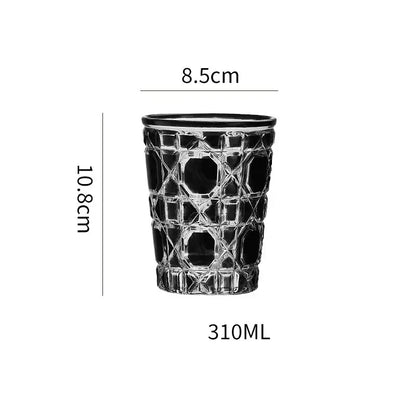A clear glass tumbler whiskey glass with a black rim and diamond cut facets in red green and amber colors