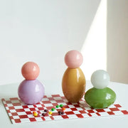Pastel-colored glossy ceramic figurines on red and white checkered surface complement geometric sphere glass vase storage container