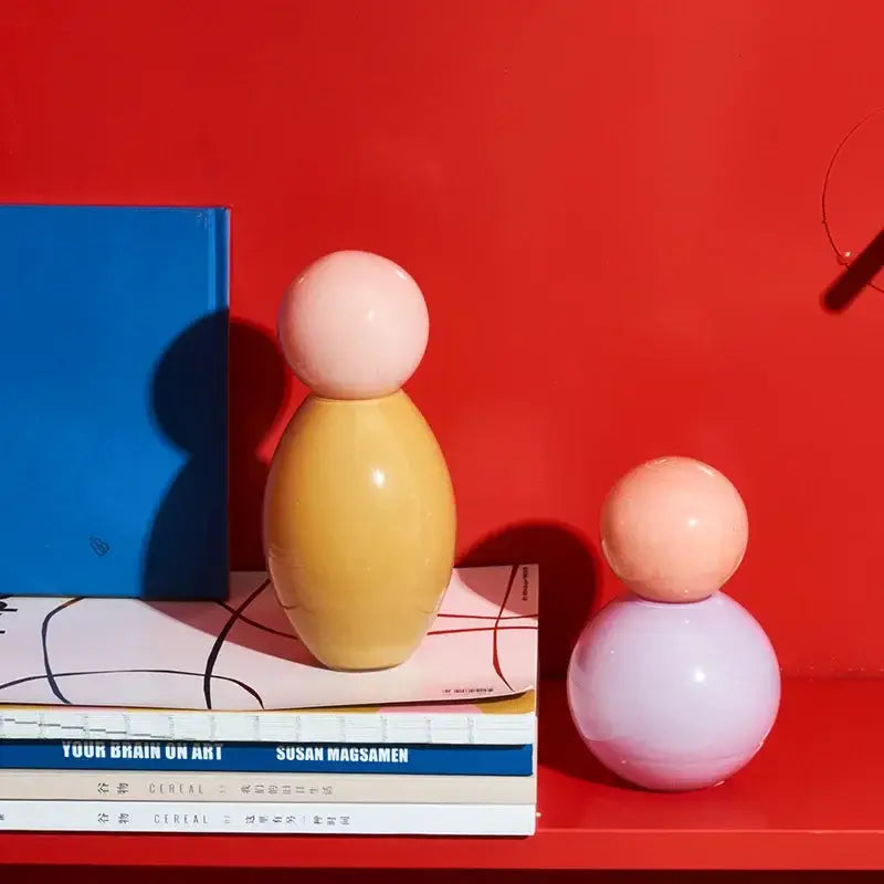 Pastel-colored ceramic figurines with smooth rounded forms complement a geometric sphere glass vase with lid for desktop storage