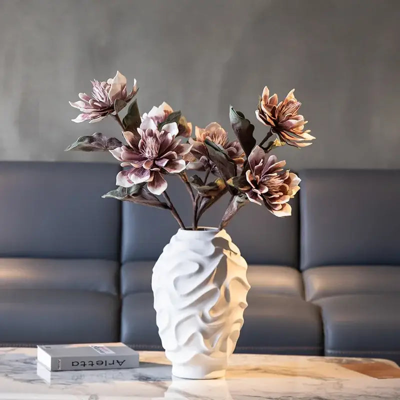White geometric spiral ceramic vase with wavy texture holding muted mauve artificial flowers for home decor