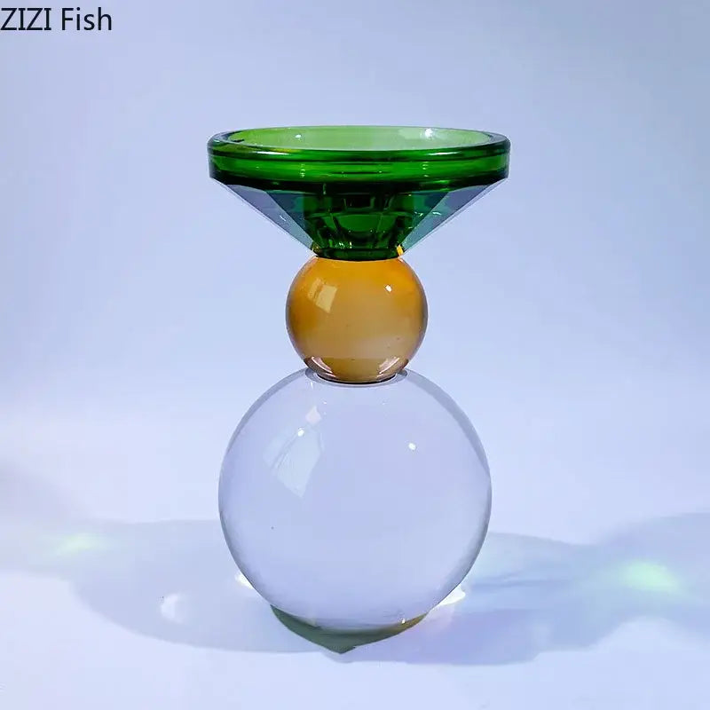 A modern geometric vibrant crystal candle holder with green faceted top, amber sphere middle, and clear crystal base
