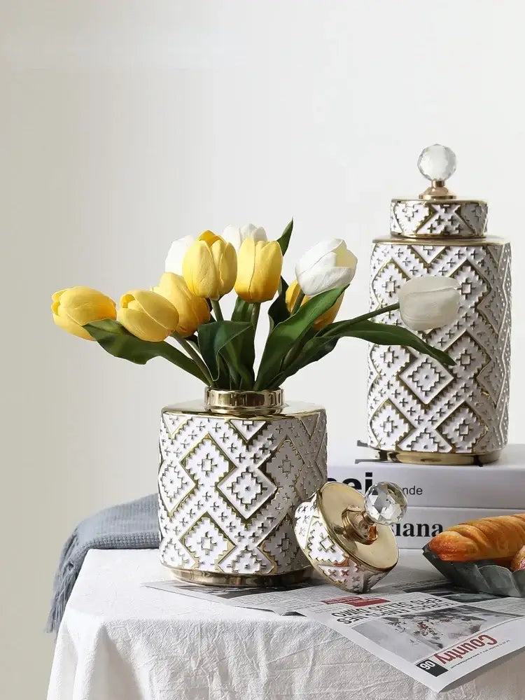 White ceramic decorative jar with golden relief geometric pattern and crystal knob holding yellow and white tulips