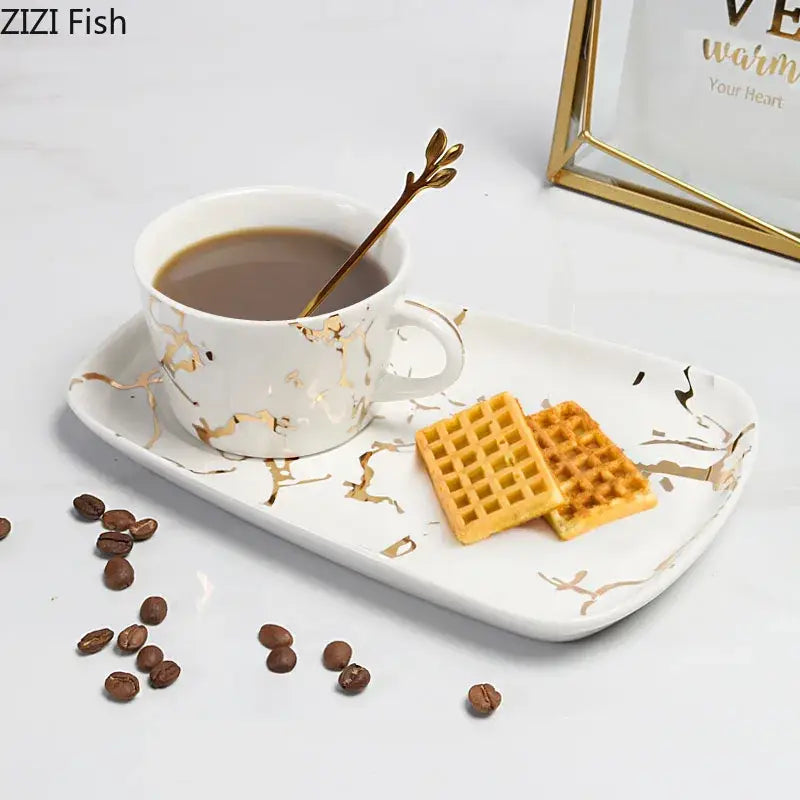 White ceramic cup and saucer set with gilded marble texture and gold leaf spoon by Decorbites for luxury dining room decor
