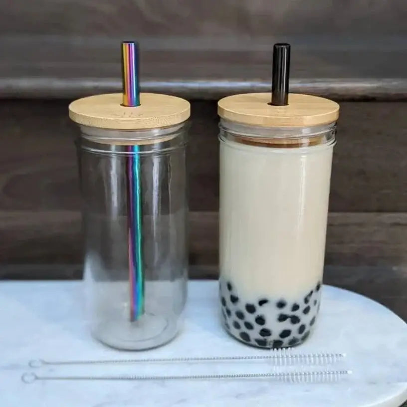 Two clear decorbites glass boba smoothie cups with bamboo lids and rainbow metal and black plastic straws