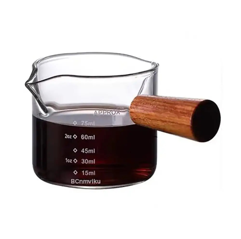Glass espresso pitcher with wooden handle filled with dark liquid and measurement markings in ounces and milliliters