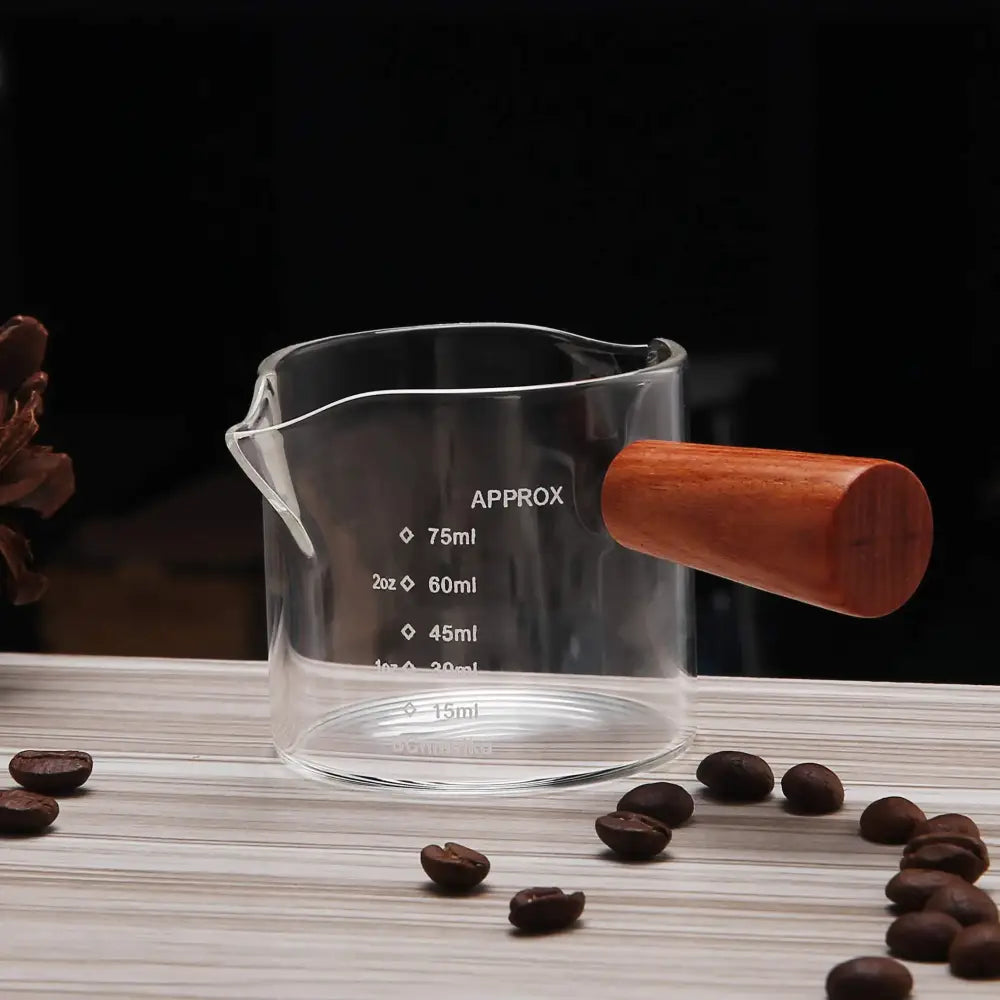 Clear glass espresso pitcher with wooden handle and measurement markings in milliliters and ounces for kitchen use
