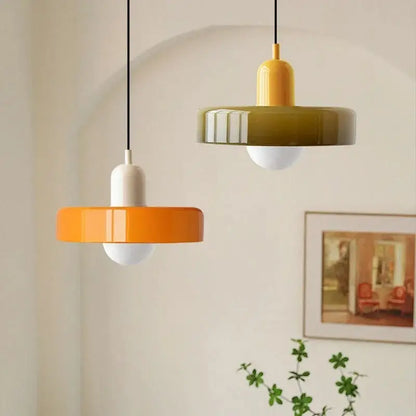 Two modern glass pendant lighting fixtures with glossy orange and olive green ceramic shades hang from black cords