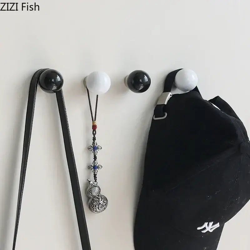 Glossy black and white ceramic wall hook clothing rack with spherical hooks holding a black cap and silver pendant