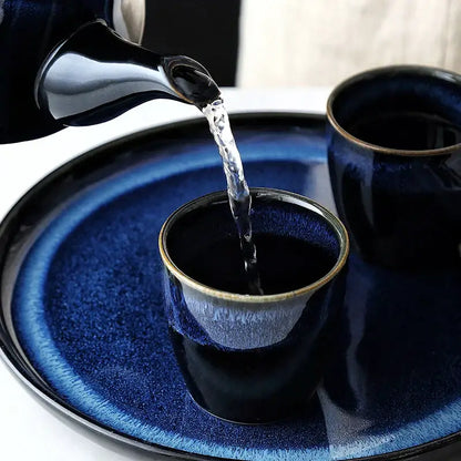 Glossy blue ceramic tea kettle set with bamboo handle pouring liquid into matching cup on a ceramic tray decorbites blue ceramic