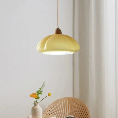 A soft yellow glossy ceramic pendant light with wooden top and cord for bedroom lighting in a pumpkin chandelier style