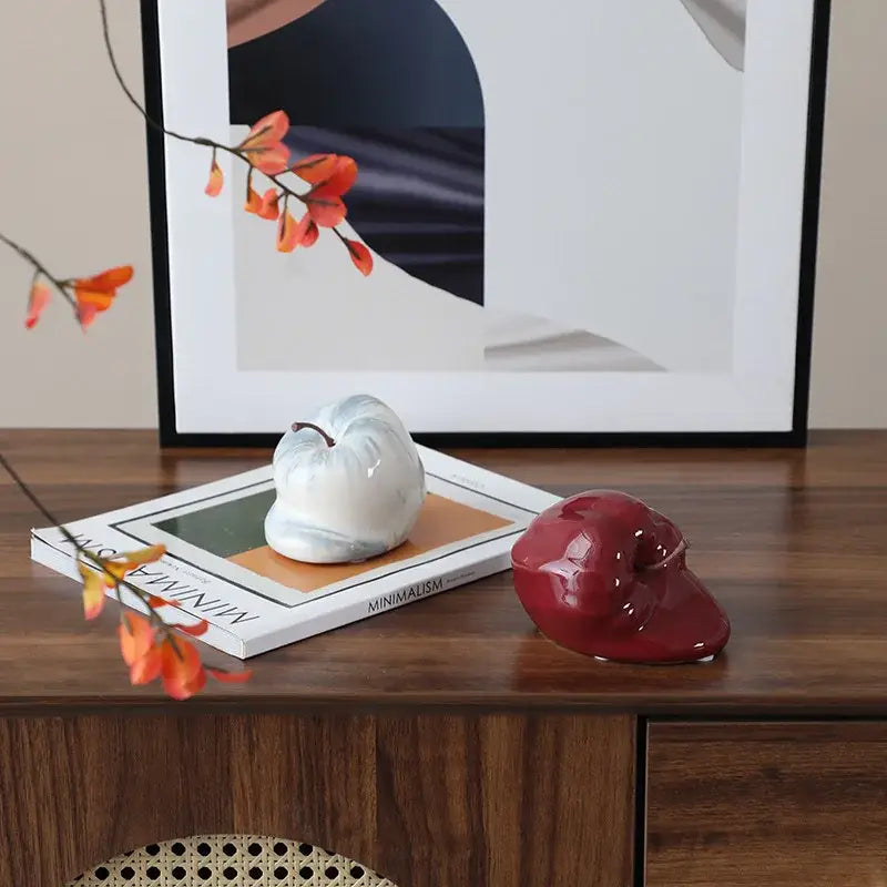 A glossy white ceramic pumpkin decor with marbled texture and dark stem resting on a magazine for abstract melting apple decorbites