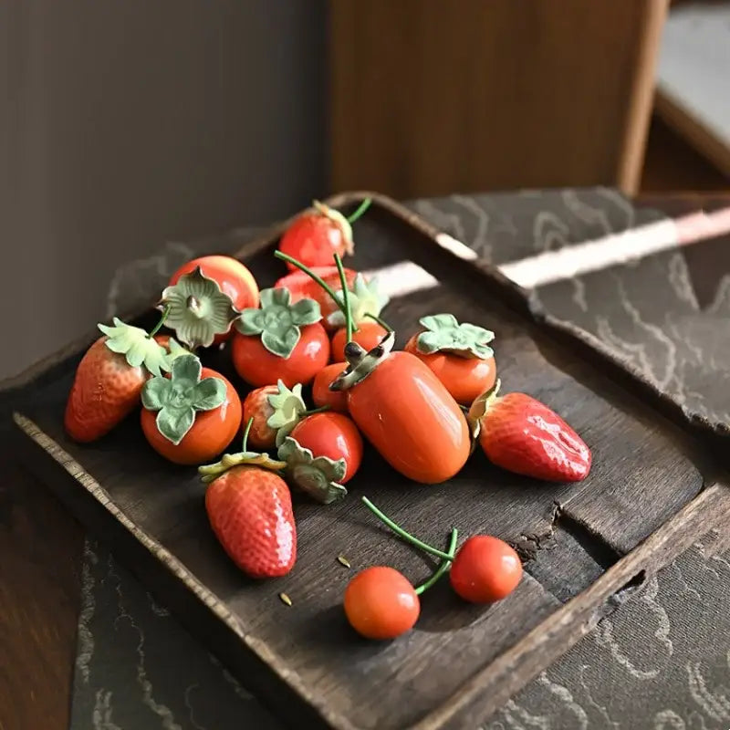 Glossy red ceramic strawberry fruit sculpture tea caddy with handcrafted persimmons on rustic wooden tray kitchen decor