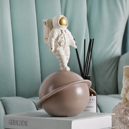 Glossy white and gold astronaut phone holder sculpture with a gold visor and backpack on a matte taupe planet globe