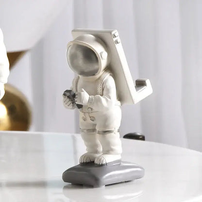 Glossy white astronaut phone holder with metallic silver helmet and backpack standing on a gray base for bedroom decor