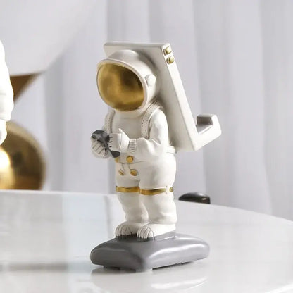 Glossy white and gold astronaut phone holder sculpture with gold visor standing on a gray base for bedroom decor