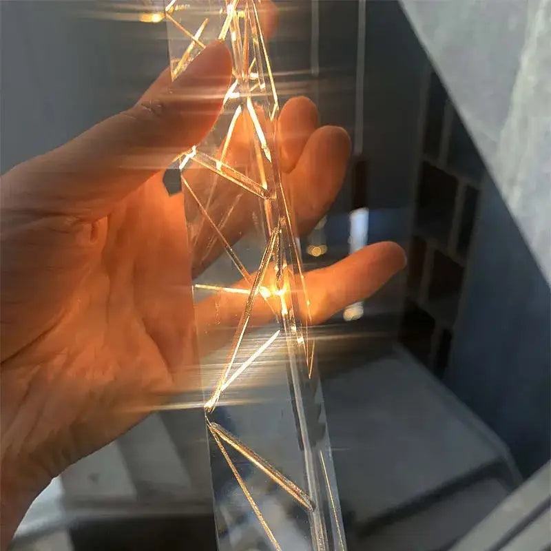 A hand holds a gold and crystal decorbites crystal led chandelier staircase light with warm golden illuminated wireframe