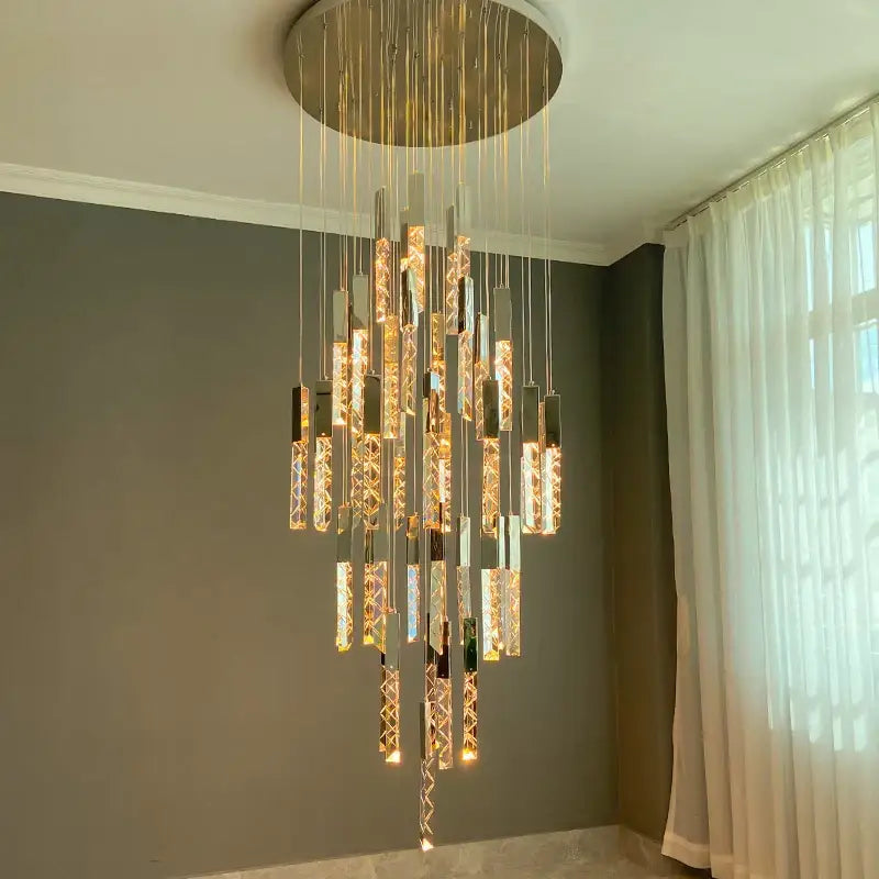 A gold and crystal led chandelier with circular gold mount and hanging rods emitting warm light for staircase decorbites crystal led