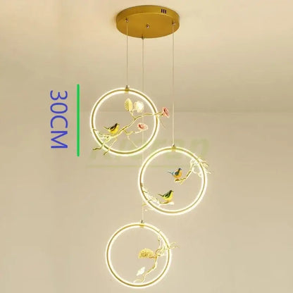 Gold-toned decorbites bird led chandelier with three hanging rings featuring floral designs for dining room lighting