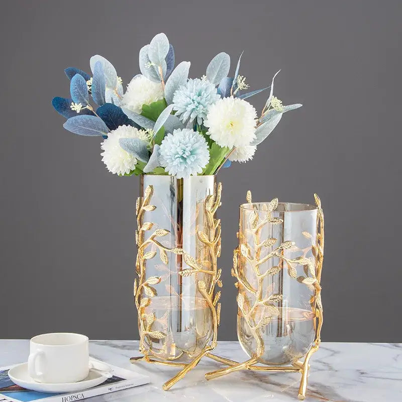 A tall clear glass vase with a gold leaf patterned metal frame and stand for coral crystal tree decor