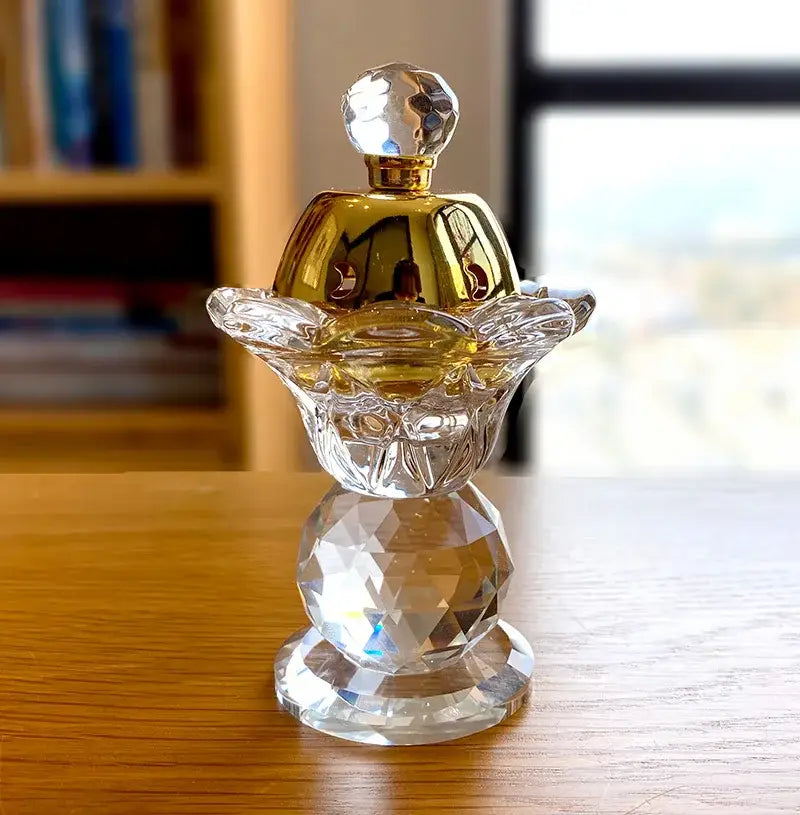 A clear crystal candle with a gold-toned cap and faceted design for elegant dining room decor and metal incense burner use