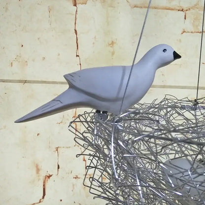 A sleek matte gray ceramic dove with a black beak perched on an intricate wire bird’s nest pendant light