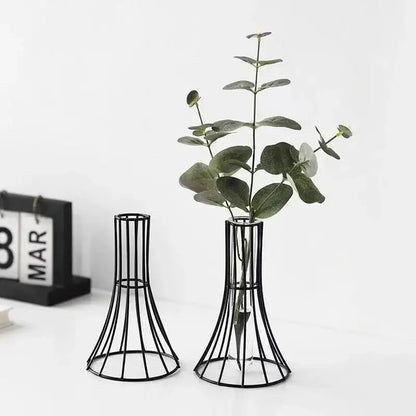 Black metal wireframe vase with flared base and slender neck holding green eucalyptus branches for modern desk decoration